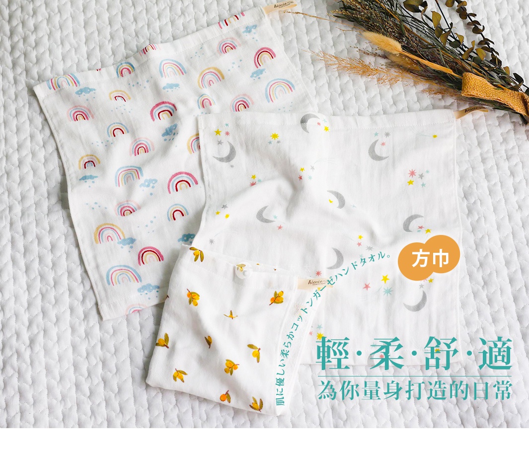 三條印有可愛彩虹、月亮星星和柑橘圖案的日本製純棉紗布方巾，平鋪在白色紋理床單上，右上方有裝飾用的乾燥花束。