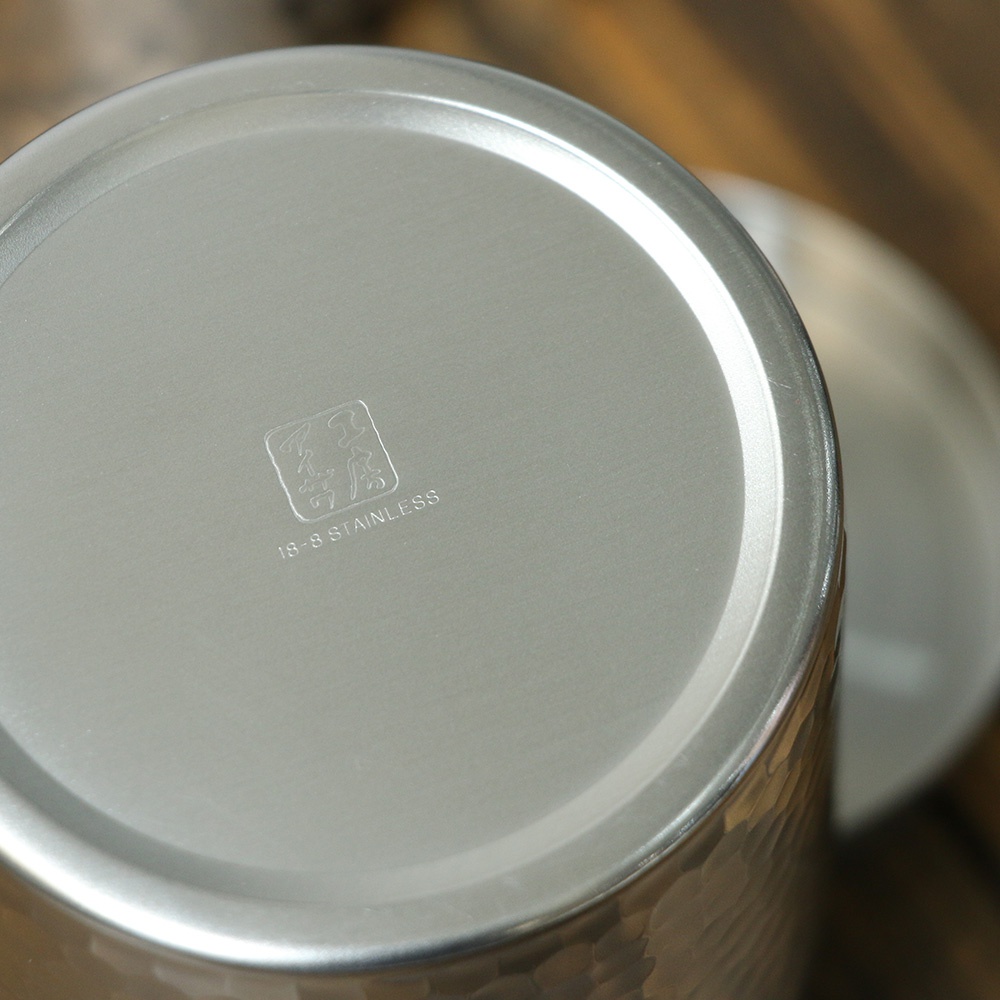 不鏽鋼錘目紋茶葉罐底部，印有「18-8 STAINLESS」字樣及品牌標誌，罐身為銀色金屬材質，表面有手工錘打紋路。