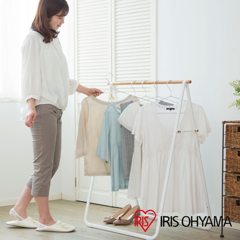 白色金屬框架的原木造型天然曬衣架，掛有淺米色、淺藍色、灰色和白色衣物，下方有兩雙高跟鞋。