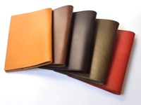 數件職人手作皮革A5筆記本書套，呈現不同顏色，包含淺棕色、深棕色、墨綠色及紅色。書套皆為皮革材質，邊緣有縫線裝飾。