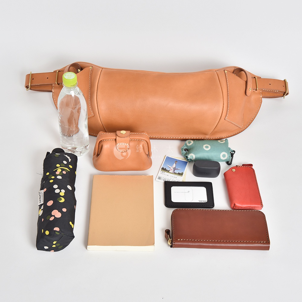一個由日本HERZ品牌生產的咖啡色皮革大容量斜背包，裡面裝有折疊傘、水瓶、小錢包、筆記本、卡夾、耳機和一個紅色卡包。