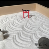 迷你枯山水模型，白色細沙上耙出波浪紋，中央立著紅色鳥居，左側有白色石塊，右下角有深色圓石及日文「枯山水」字樣。