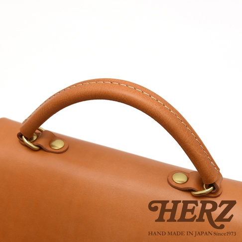 HERZ 品牌標誌與製造地，特寫箱包棕色皮革提把與金屬配件