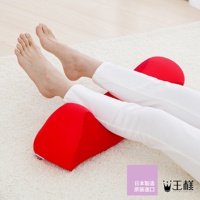 一對紅色的舒背拉伸枕，置於鋪有白色絨毛地毯上，一位穿著白色長褲的人的雙腿屈膝置於枕上。