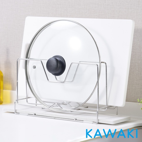 銀色金屬架上放置著一個透明玻璃鍋蓋，鍋蓋中心有黑色圓形提把。鍋蓋後方是白色長方形砧板，砧板底部有一塊淺灰色珪藻土瀝水板。