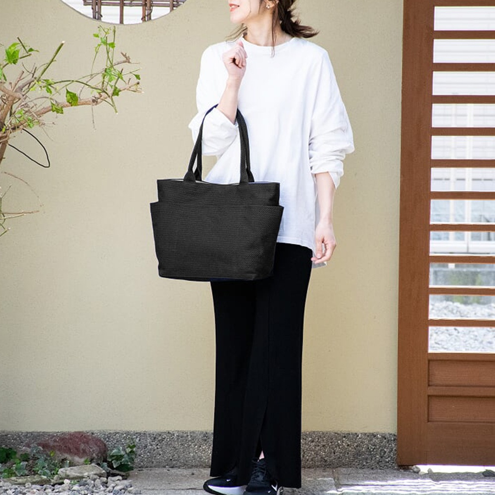 一位女性提著黑色三河木綿刺子織手提托特包，包包具有兩個側邊口袋。