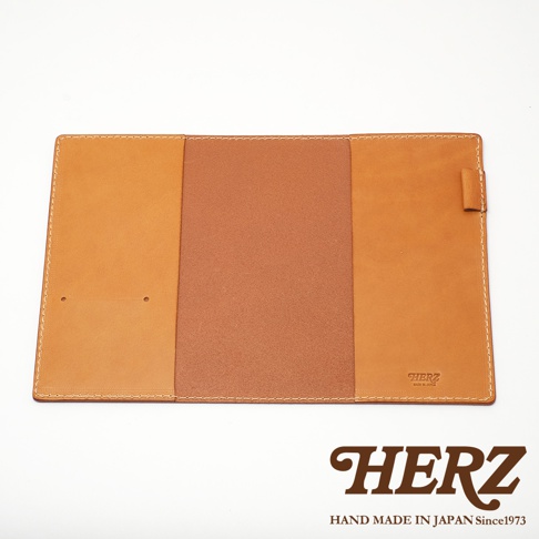 職人手作皮革B6記事本書套，採用棕色皮革，內有兩個卡槽，表面有明顯的縫線，右側有一條皮革束帶。