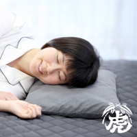 一位女性側臥在灰色枕頭上，枕頭平放在菱格紋床墊上。女性身穿白色睡衣，頭部輕靠在枕頭上，閉眼並露出微笑。