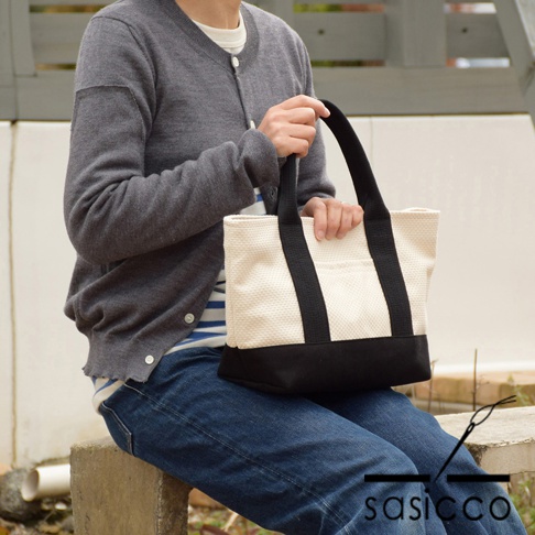 一位女士手持米白色三河木綿刺子織迷你托特包，包身底部為黑色。