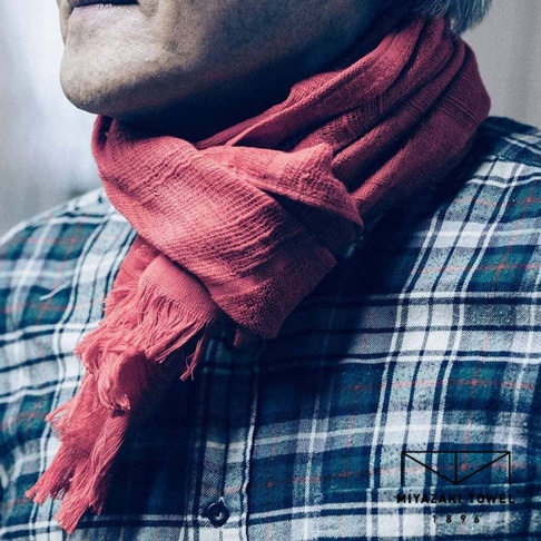 紅色今治匹馬棉圍巾，材質輕薄，帶有流鬚裝飾，圍繞在穿著藍色格紋襯衫的人物頸部。