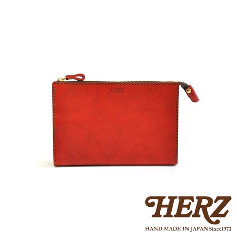 紅色皮革製成的職人手作三角底拉鍊手拿包，表面有品牌壓印，搭配金色拉鍊頭，整體風格簡約。