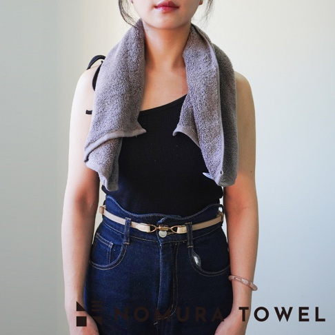 野村毛巾 YABAI 水漾瞬吸厲害半浴巾，女性身著黑色細肩帶背心、深藍色牛仔褲和米色皮帶，頸部圍著一條灰色毛巾。