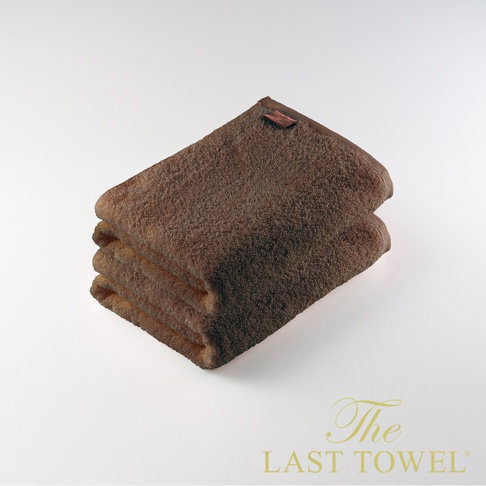 兩條咖啡色純棉柔浴巾疊放，頂部浴巾有一褐色品牌標籤，材質蓬鬆柔軟。