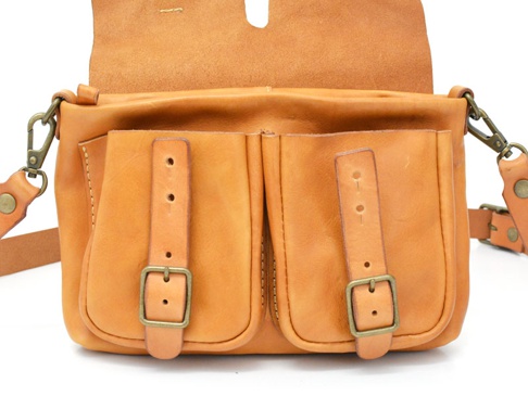 職人手作皮革水洗加工前雙口袋肩背包，天然棕色皮革，正面有兩個帶有銅扣和皮帶的翻蓋口袋，皮革材質，附有可調節的肩帶和金屬扣環。
