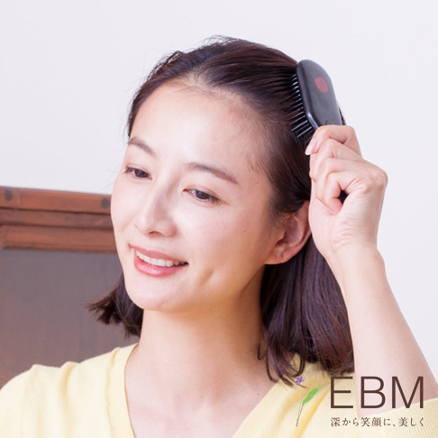 女性使用黑色E.遠紅外線能量梳梳理頭髮，梳子為橢圓形，帶有紅色標誌。