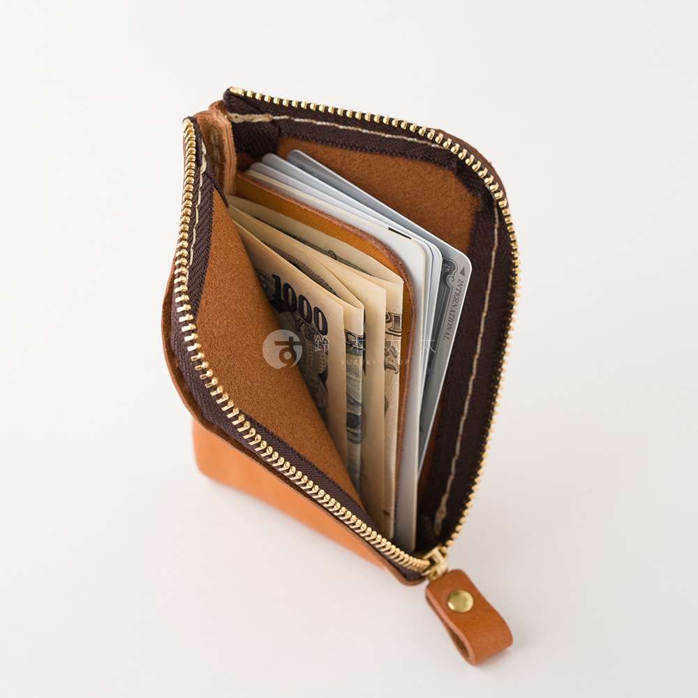 一個打開的棕色皮革迷你錢包，內部配有分隔層，收納著幾張銀行卡和日本千元鈔票，拉鍊處附有皮革拉環，整體呈現簡約精緻的手工皮革質感。