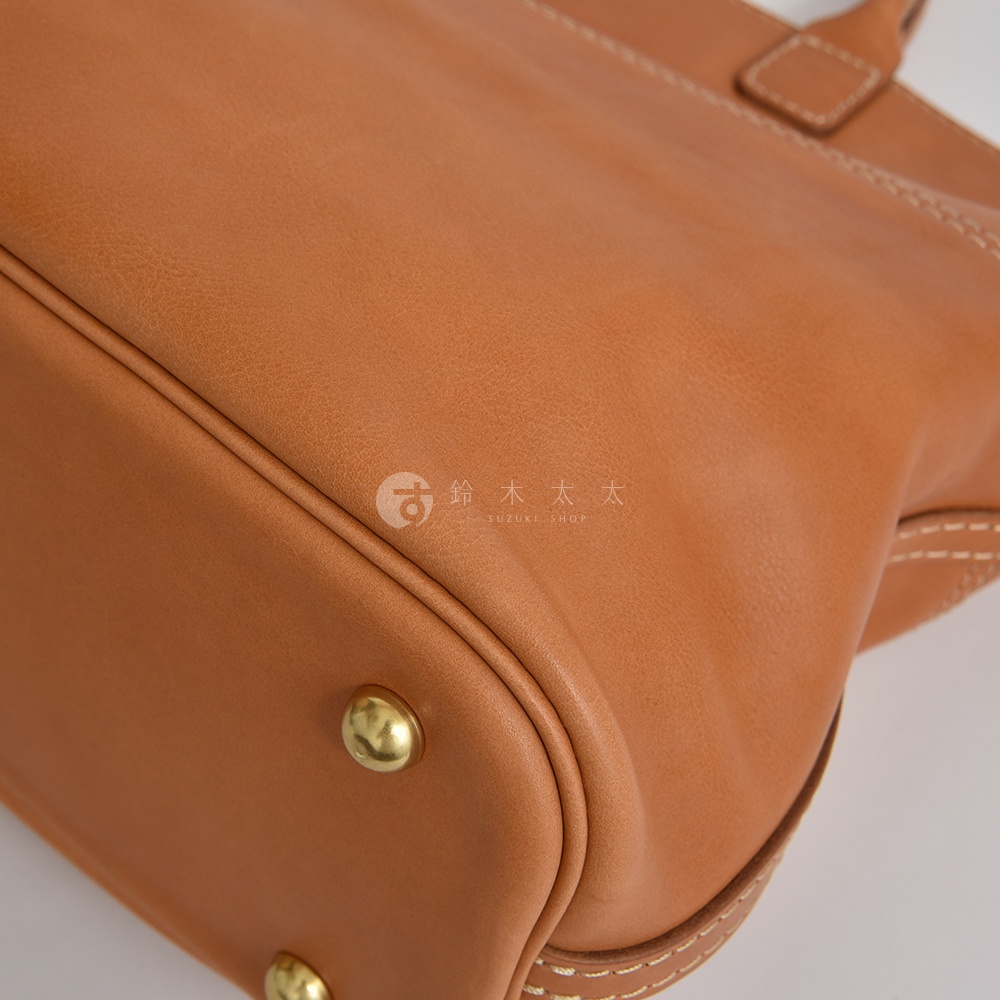 棕色皮革兩用托特包，特寫包包底部與側面，展示縫線細節及金屬腳釘。