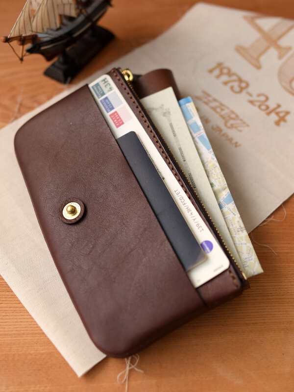 深棕色皮革長夾，內含護照、機票及其他旅行文件，配有金色金屬鈕扣及拉鍊。