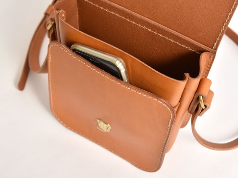 棕色皮革迷你翻蓋單肩包，包身縫線清晰，正面有金色金屬扣飾。包內可見手機，並有分層設計。