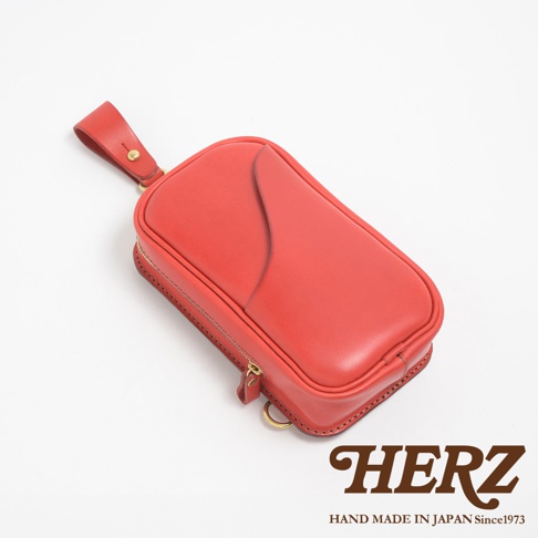 日本 HERZ 品牌紅色皮革製作的兩用直立型斜背包，包包帶有拉鍊，旁邊有品牌 logo。