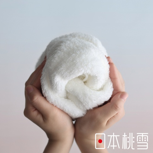 兩隻手捧著一條捲起來的白色蓬鬆毛巾，背景為淺灰色，右下角有日本桃雪的標誌和文字。
