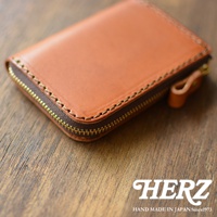 職人手作的棕色皮革拉鍊短夾，拉鍊為金色，邊緣有縫線裝飾。