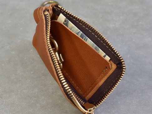 棕色皮革製的職人手作鑰匙包，拉鍊打開，露出內部可放鈔票和鑰匙的隔層，以及金屬鑰匙圈。