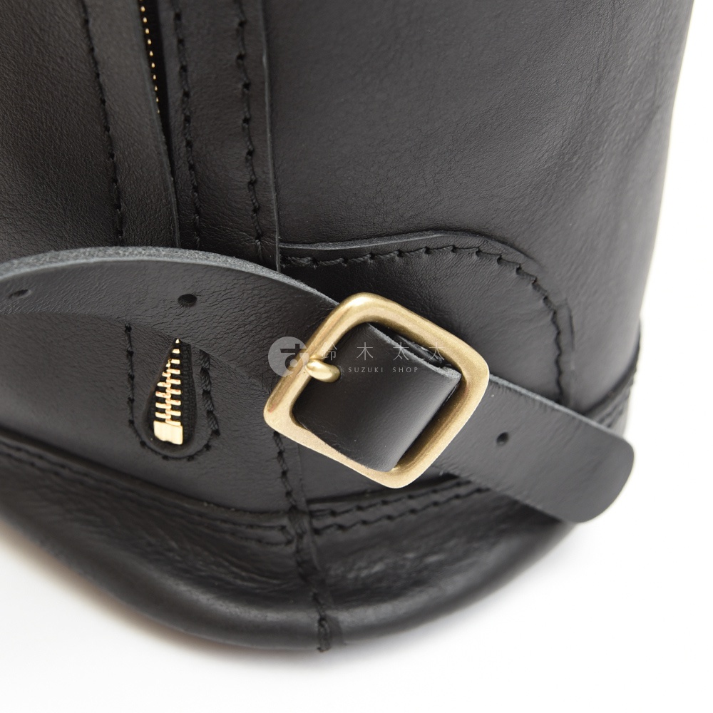 黑色皮革束口後背包，特寫金屬拉鍊與方形金屬釦環，皮革質感細膩，縫線工整。