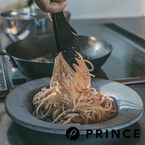 黑色萬用料理麵食分菜夾，夾著一盤義大利麵，麵條上灑有細碎的配料。
