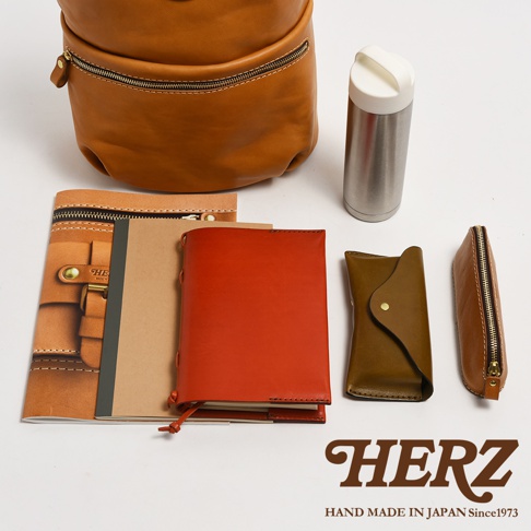 淺棕色皮革後背包、銀色保溫瓶、紅色筆記本、棕色皮革筆記本套、深棕色皮革眼鏡盒和長方形皮革筆袋。