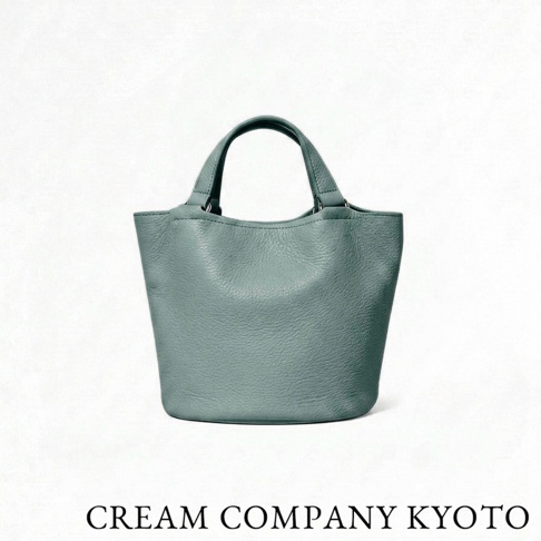 一款由京都品牌 CREAM COMPANY KYOTO 出品的迷你水桶托特包，採用灰綠色荔枝紋牛皮革製成，設計簡約輕巧，展現職人手作質感。