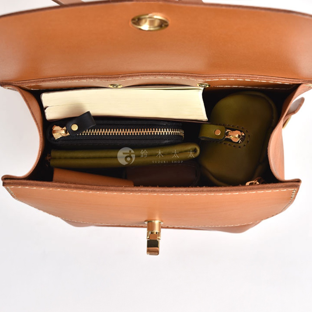 棕色皮革翻蓋迷你後背包，內部裝有書籍、黑色長夾、綠色零錢包及其他小物，展示包款的收納空間。