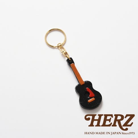 職人手作皮革吉他造型鑰匙圈，黑色吉他主體搭配棕色琴頸，點綴紅色與橘色音孔細節，附有金色鑰匙圈。