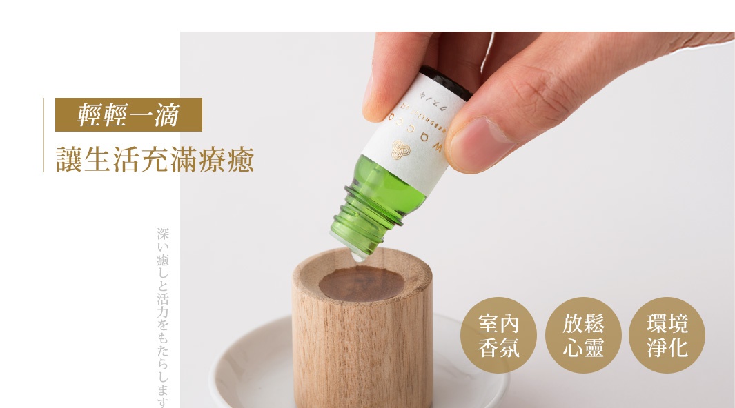 一隻手拿著青森HIBA檜木精油小玻璃瓶，瓶身為綠色，瓶口滴出一滴精油，落入木質擴香座中。