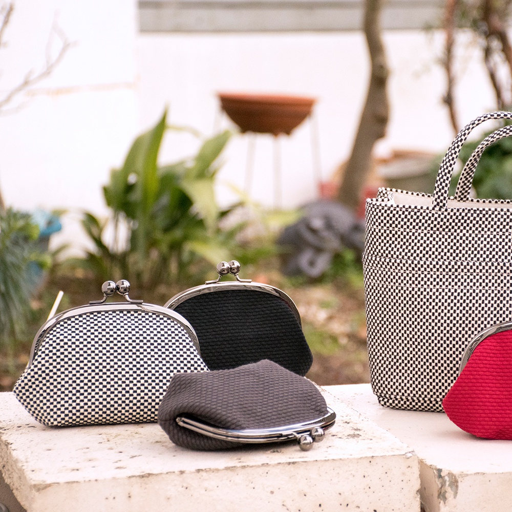 三河木綿刺子織口金零錢包，有黑白格紋、純黑、深灰及紅色四種款式，造型皆為弧形，配有金屬釦。