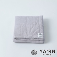 一條淺灰色、表面有格紋縫線的毛巾，材質為脫脂棉混紗，邊緣有細緻的車縫線，角落處有一個印有「YARN HOME」字樣的白色標籤。
