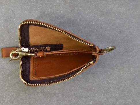 職人手作皮革Organ抽繩收納鑰匙包，以棕褐色皮革製成，設有拉鍊開合，內含一個小拉鍊袋，外側有皮革抽繩及金屬掛鉤與鑰匙圈。