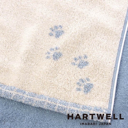 這是一條 HARTWELL 今治午睡貓咪系列雙色浴巾，整體為米白色與藍色拼接設計，毛巾表面上有幾處藍色的貓爪印圖案，角落印有 HARTWELL IMABARI JAPAN 品牌字樣，呈現質感舒適的日系毛巾風格。