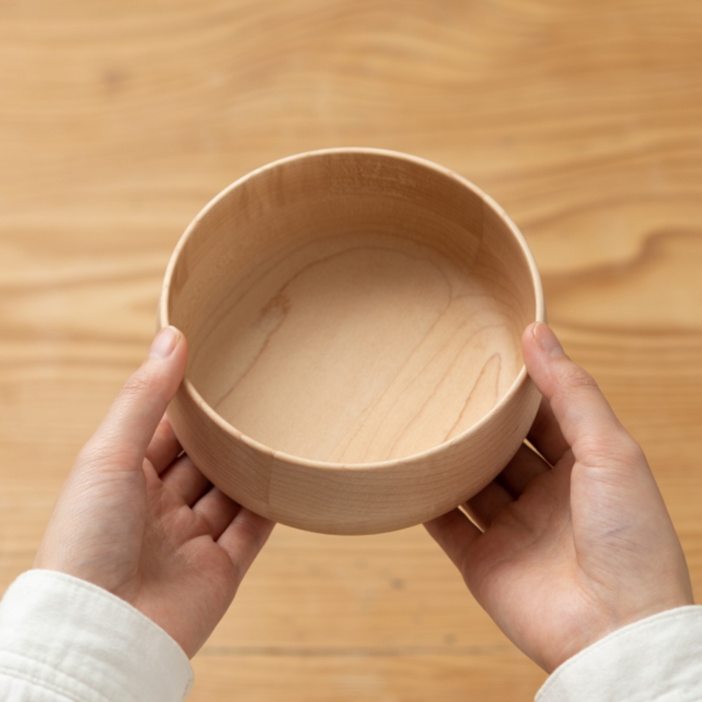 一隻手捧著一個淺色的圓形楓木沙拉碗，碗內呈現自然的木紋。