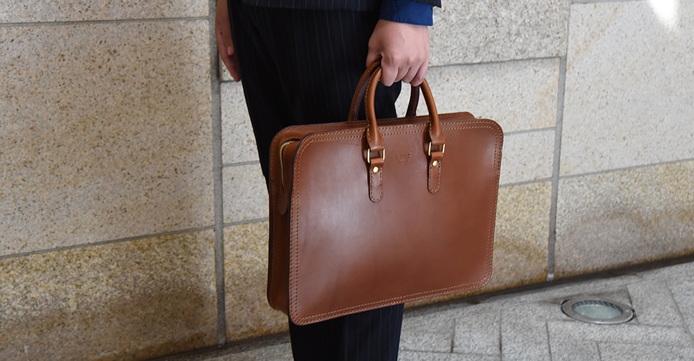 棕色皮革手提公事包，配有金色釦件和雙提把，展現精緻工藝。