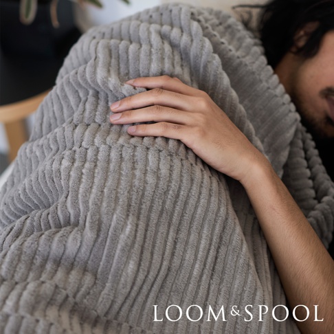 一件淺灰色立體直紋純棉單人毯，觸感柔軟，有細緻的條紋紋理，被一位男子蓋在身上。