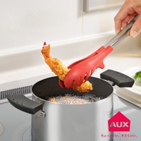 紅色的 UCHICOOK 不沾桌快手料理夾，夾著一塊炸好的蝦，上方有銀色的金屬手柄，下方是正在烹飪的鍋具。