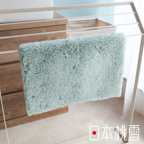 日本桃雪出品的淺綠色絨毛浴墊懸掛在晾衣架上，下方地面是六角形白色地磚。