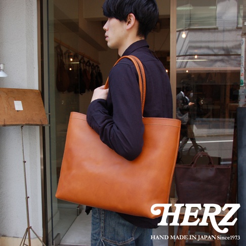 一位男士身穿深色上衣，肩背一個大容量的棕褐色皮革托特包。