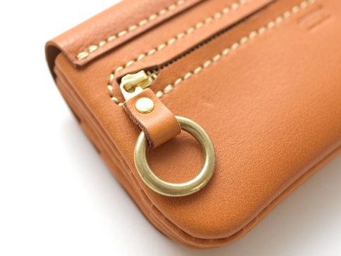 棕褐色皮革長夾，特寫拉鍊和金屬環細節，縫線清晰。