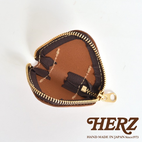 日本職人手作HERZ棕色皮革三角飯糰造型零錢包，呈現內部拉鍊結構與細緻車縫工藝，包體採用Latigo軟皮革材質，右下角印有品牌標誌與產地說明。