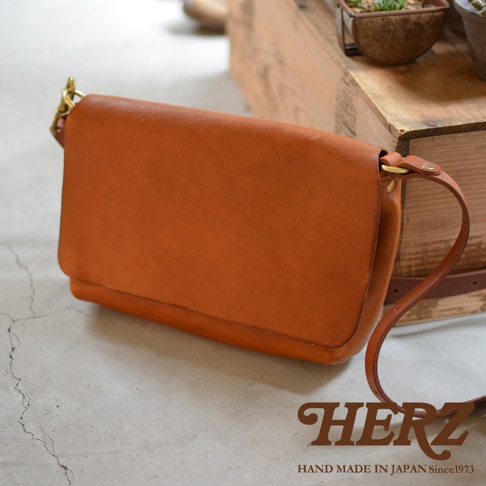 一個棕色皮革斜背包，上面印有HERZ字樣和HAND MADE IN JAPAN Since1973字樣。