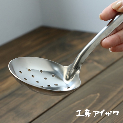 一只手正握著一個不鏽鋼中型撈勺，勺面有許多圓形孔洞，勺柄呈流線型。