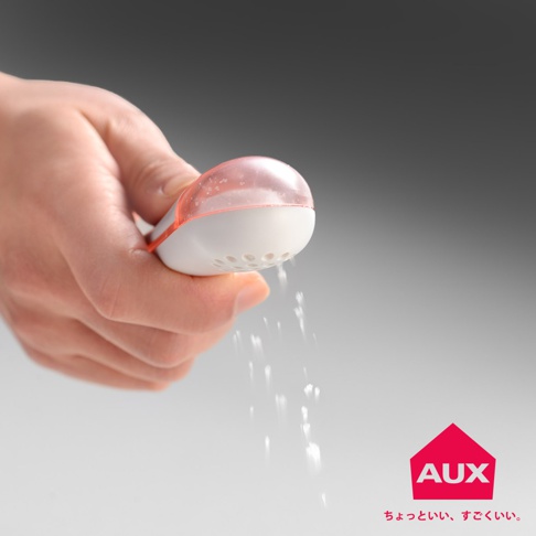 手持白色撒鹽器，其透明粉紅色蓋子內有鹽粒，底部有圓形孔洞，正傾斜撒出細鹽。