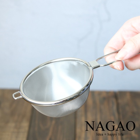 一只手正握著一個不鏽鋼製的細網濾茶器，濾網為銀色，網孔極細，帶有一個銀色金屬手柄。